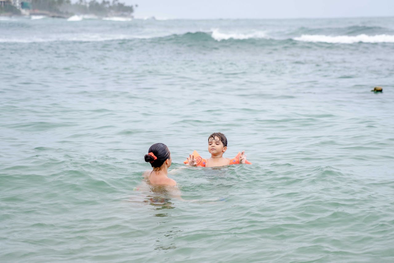 A mother and her child swim in the ocean, enjoying a relaxing day at the beach.
