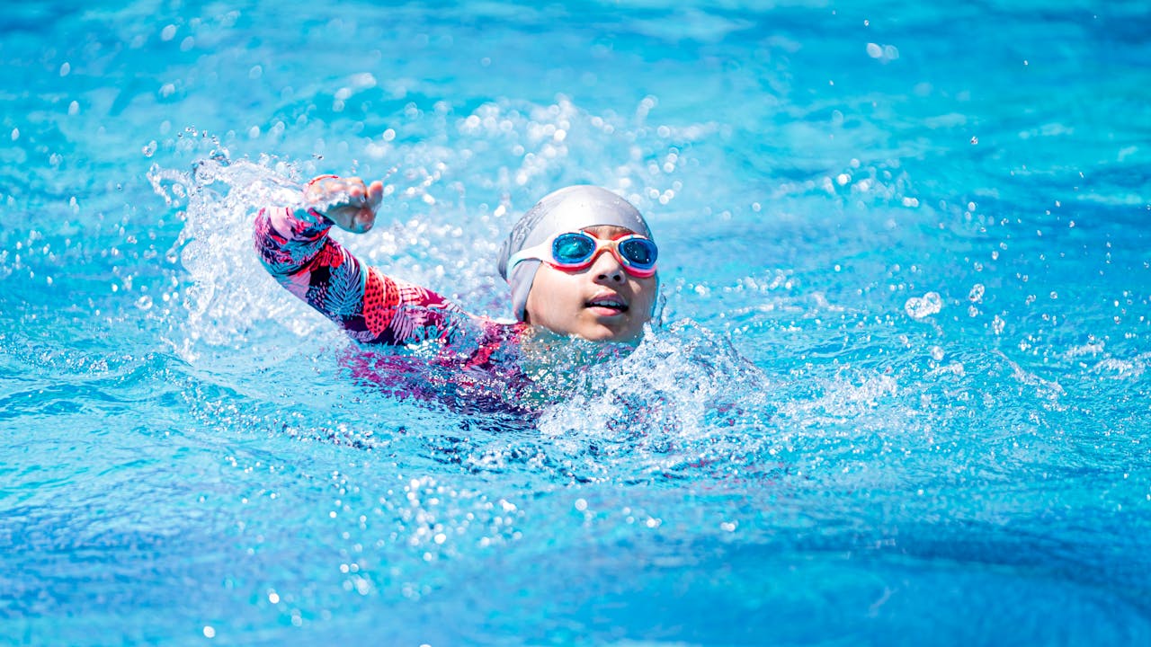 A young swimmer in goggles and cap performing freestyle stroke in a vibrant blue pool.