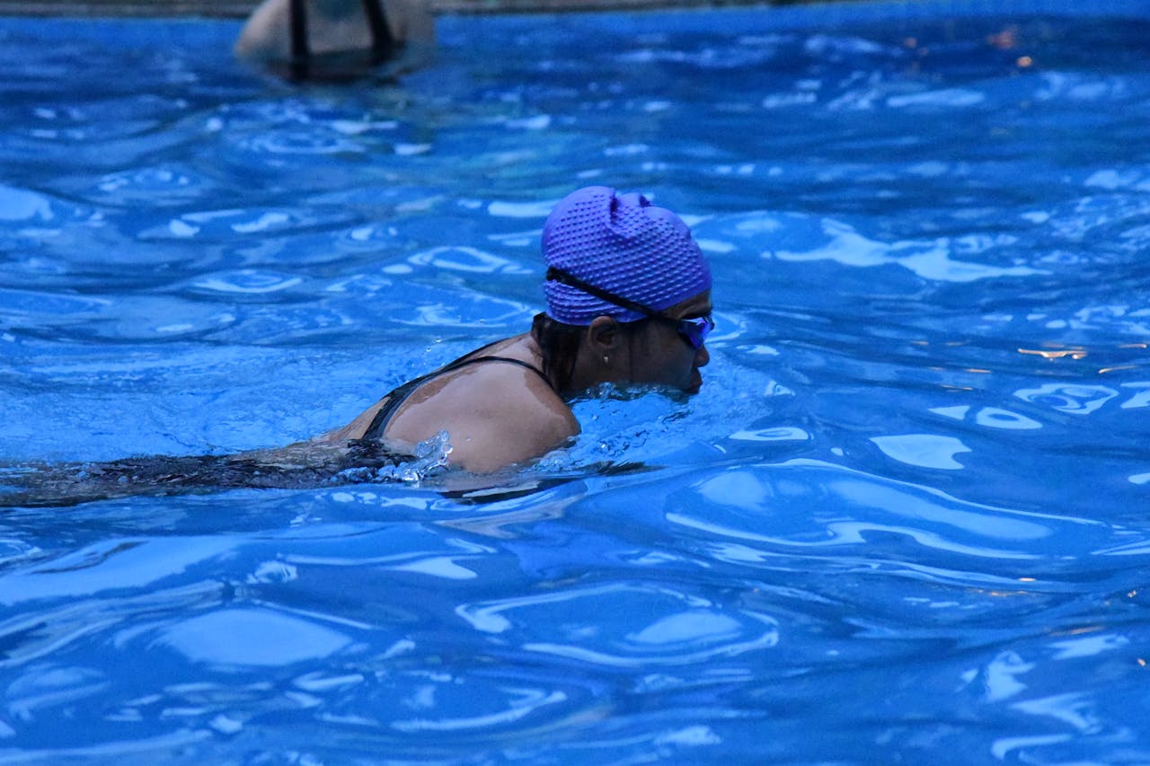 An adult female swimmer practicing in a pool, wearing goggles and swim cap.