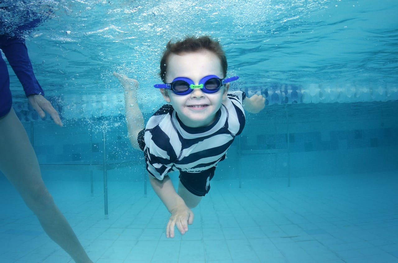 Young boy happily swims underwater in a swimming pool wearing goggles. Summer fun captured.